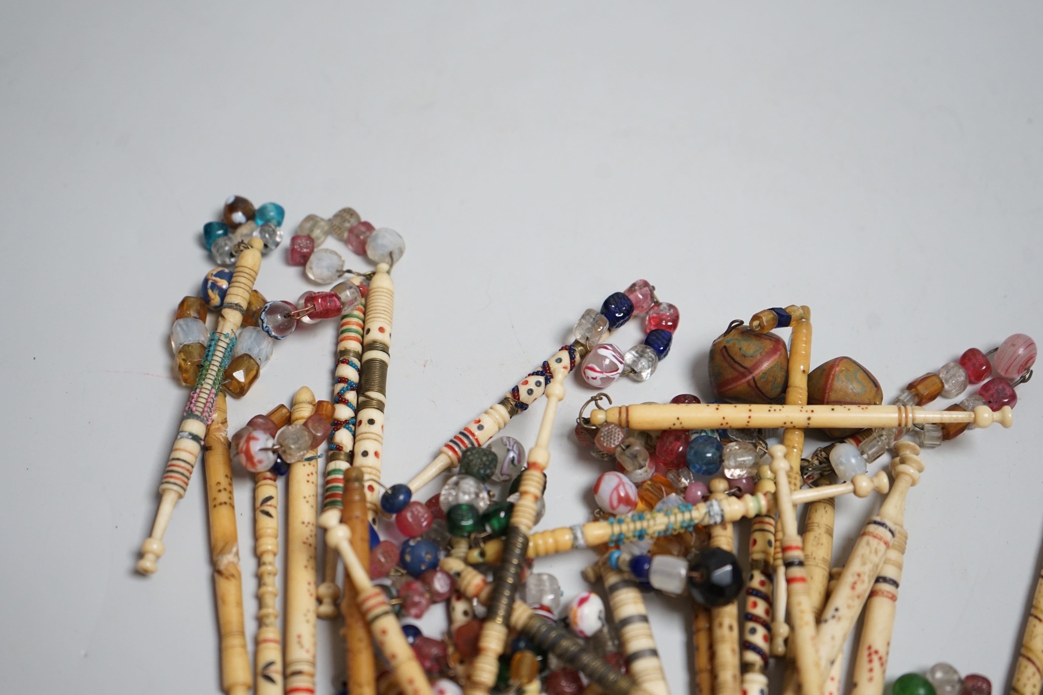 Twenty 19th century ornately decorated lace bobbins with glass bead tops and eleven carved bobbins with indistinctly carved surnames and names